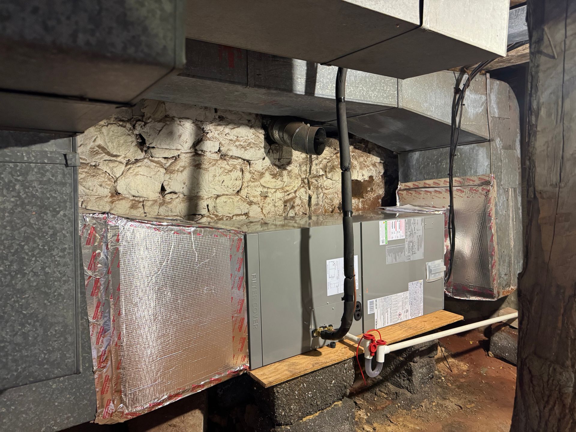 Basement wall with HVAC ducts and insulated metal panels, showing exposed stone and foam insulation.