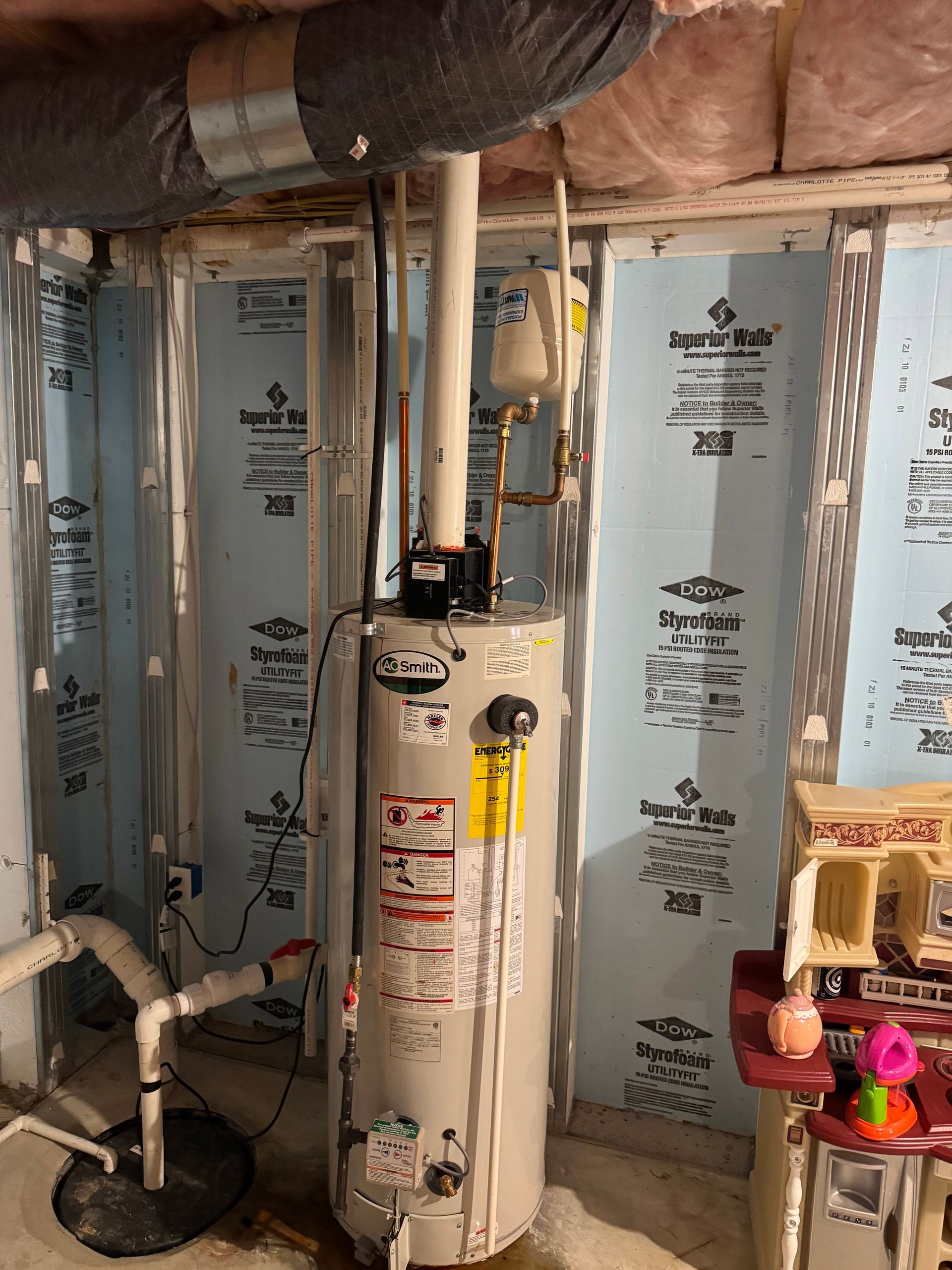 Basement utility area with a water heater, pipes, insulation, and a sump pump.