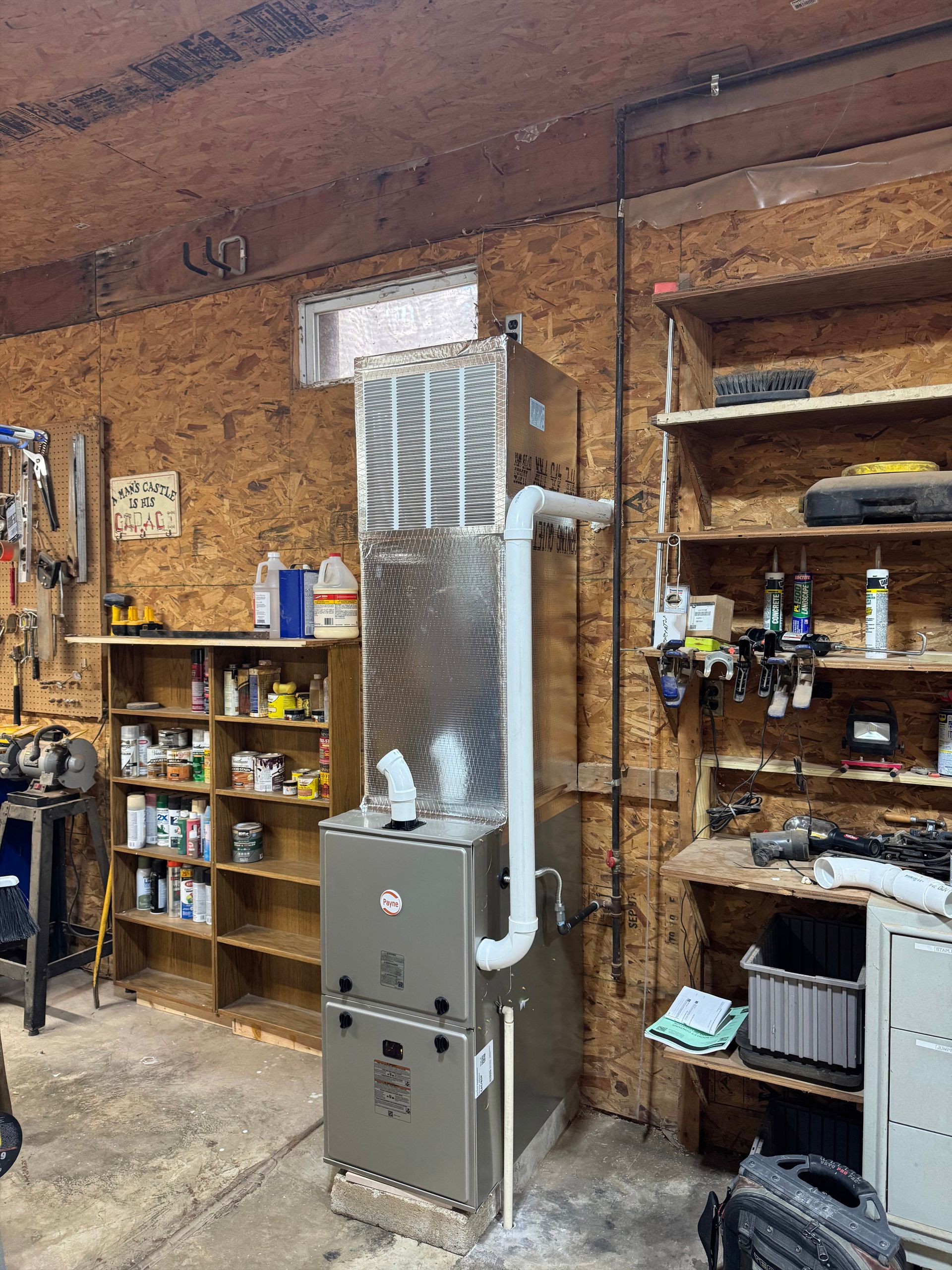 Workshop wall with a tall gray HVAC unit, shelves, tools, and exposed brick.