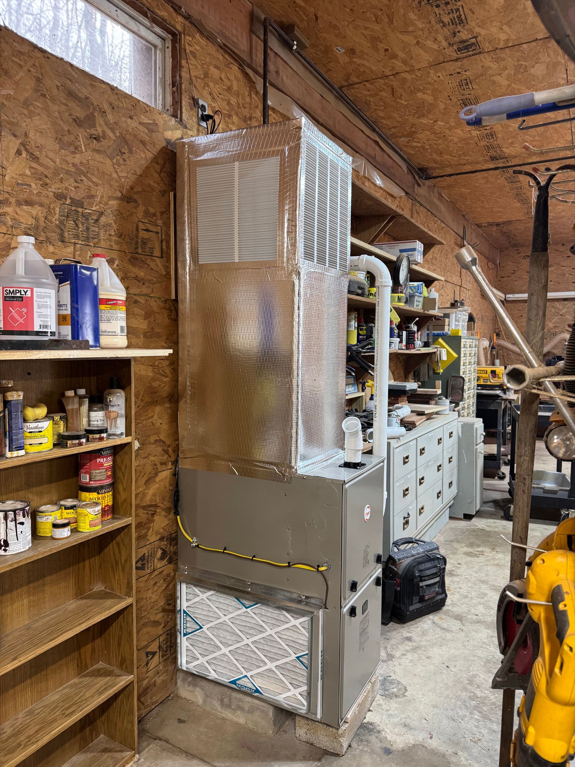 Insulated HVAC unit in a cluttered workshop with shelves, tools, and brick walls