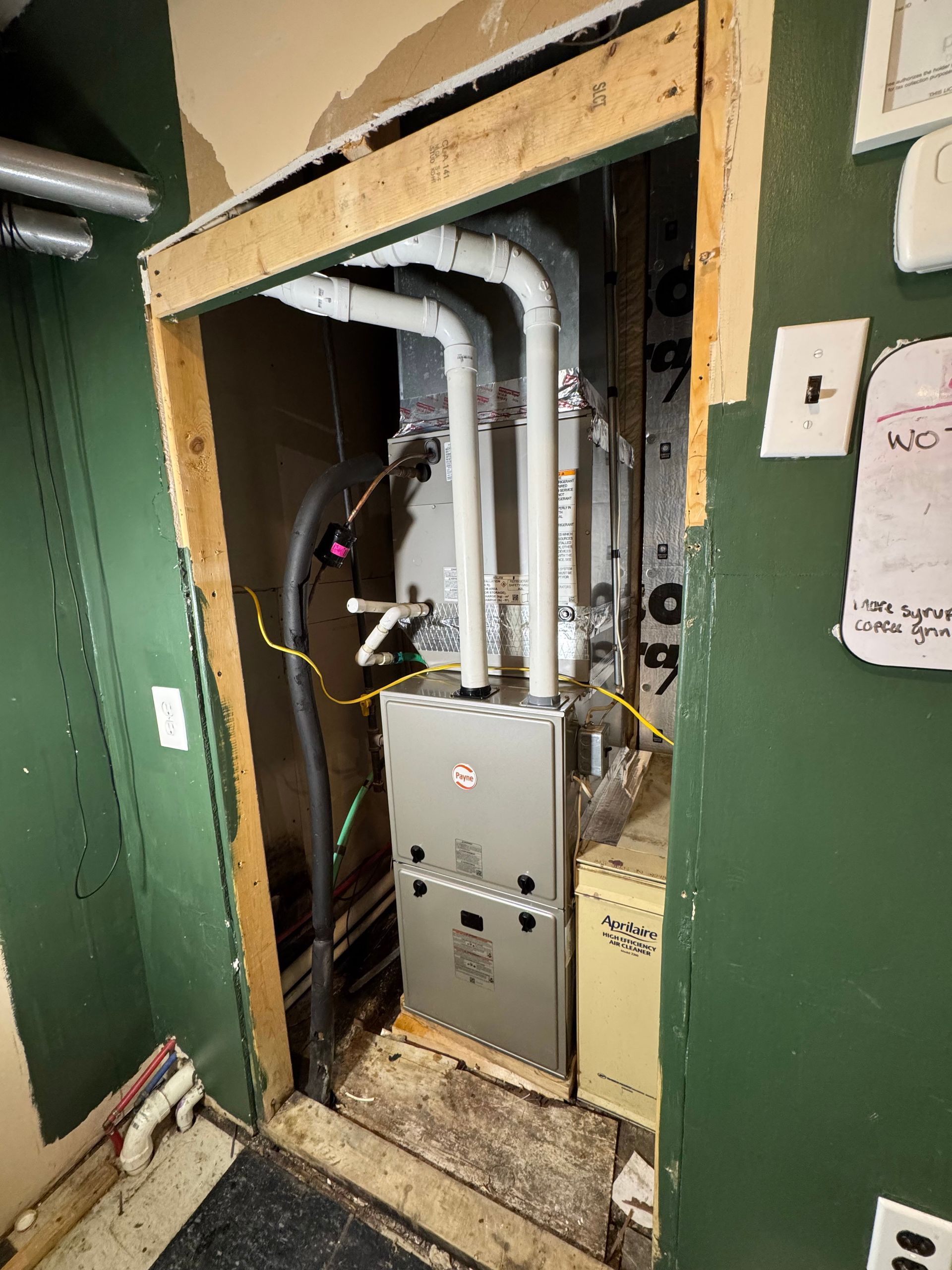 Open utility closet with metal ducts and electrical panel in a green hallway