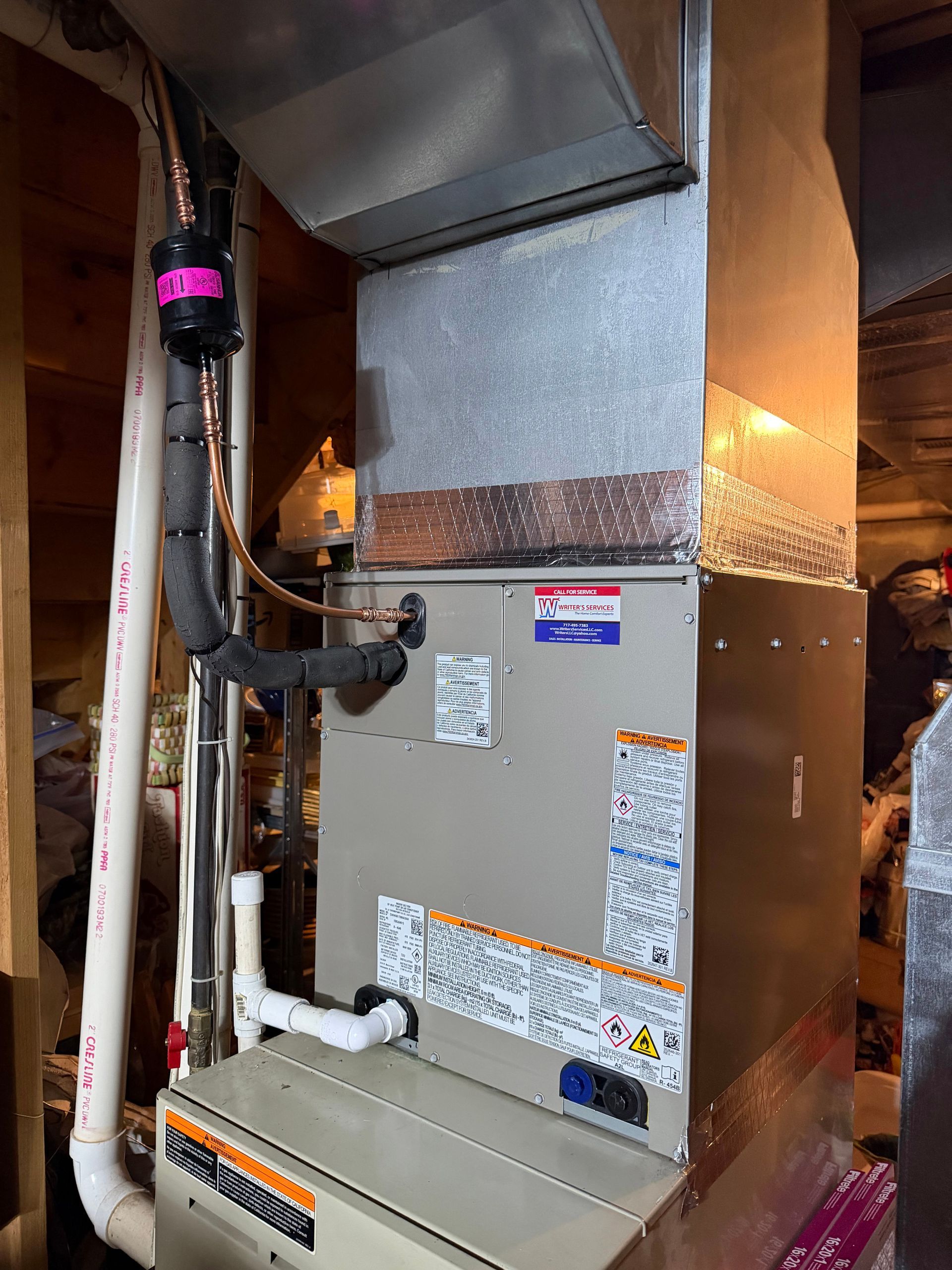 Furnace and HVAC ductwork in a utility closet, with gray metal unit and exposed pipes.
