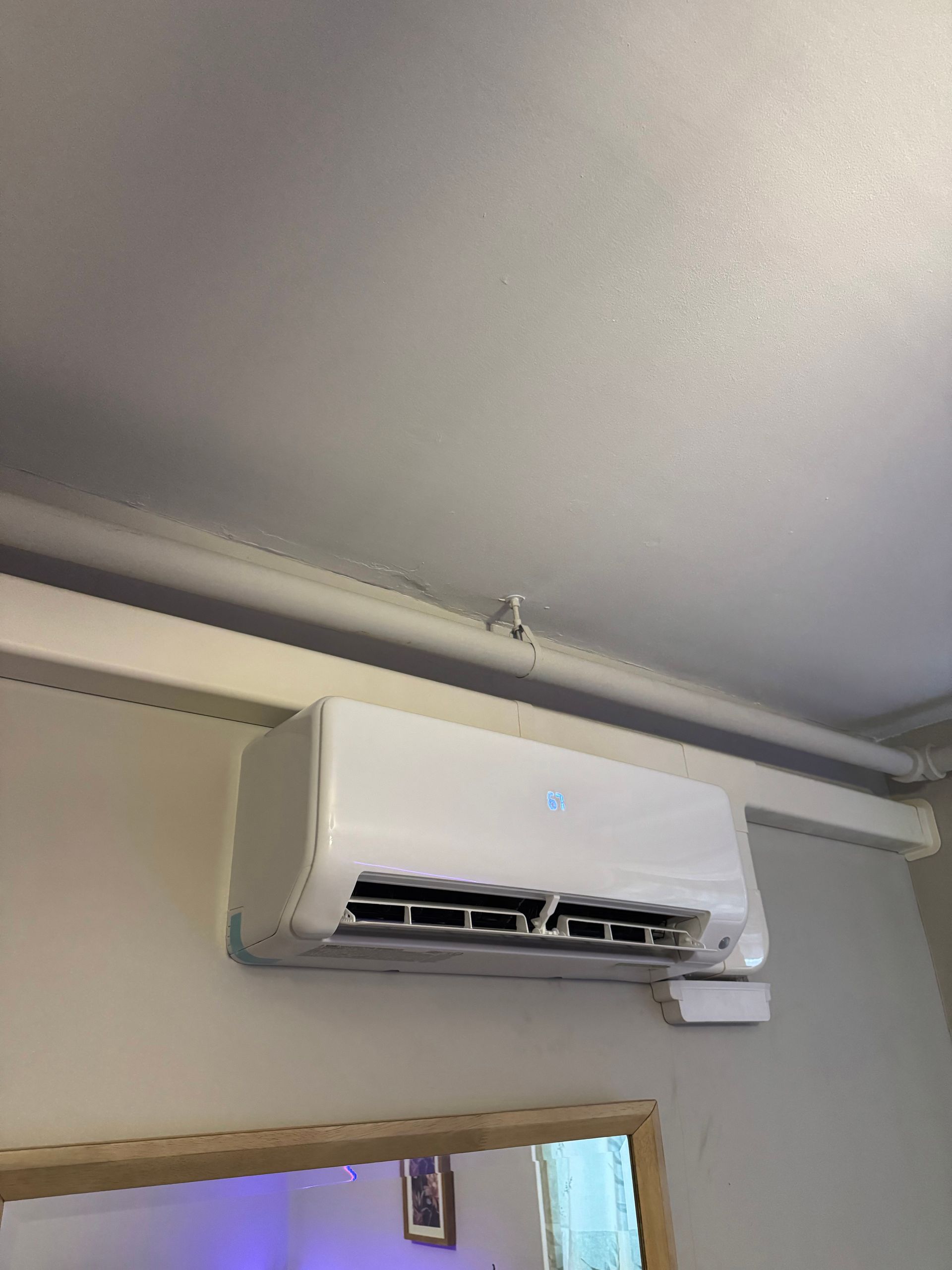 Wall-mounted white air conditioner above a doorway in a beige room