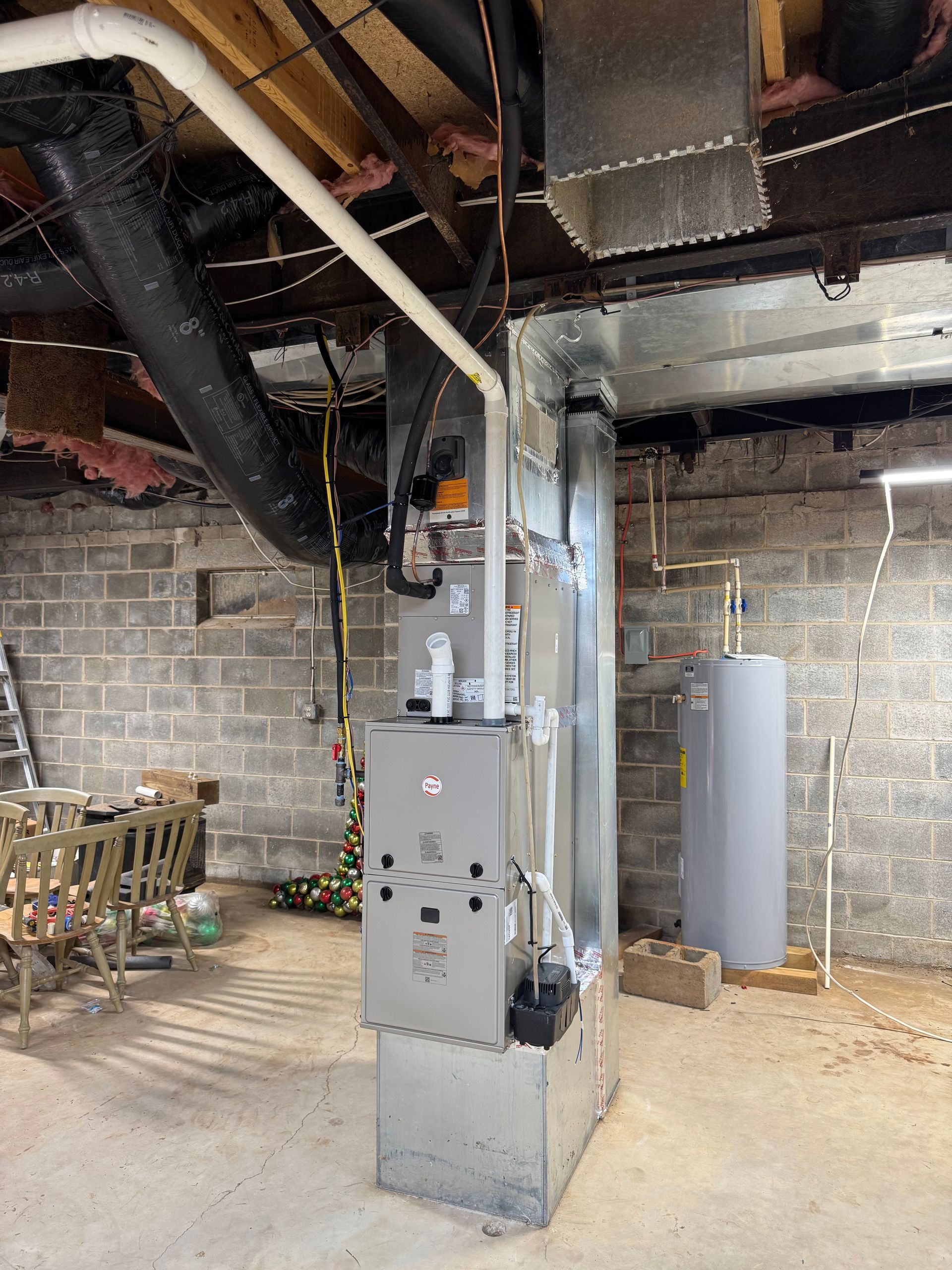 Basement utility room with a gray furnace and exposed ductwork under open ceiling joists