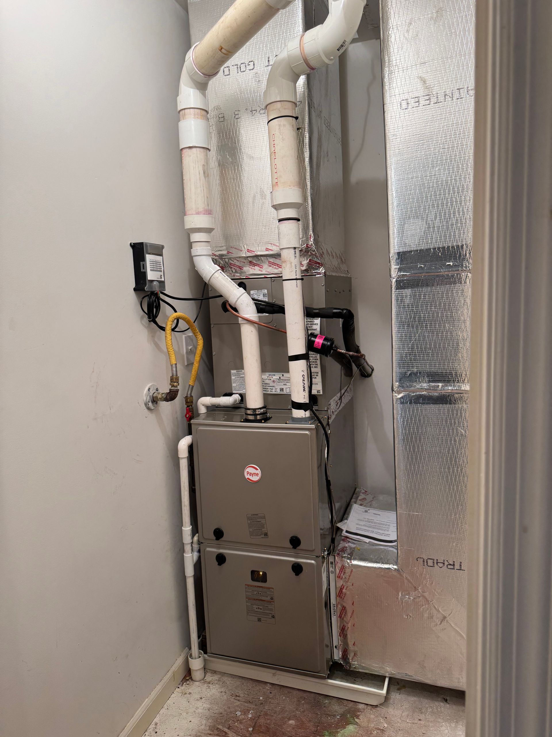 Indoor HVAC furnace with white insulated ducts and foil-lined wall panels in a utility closet.