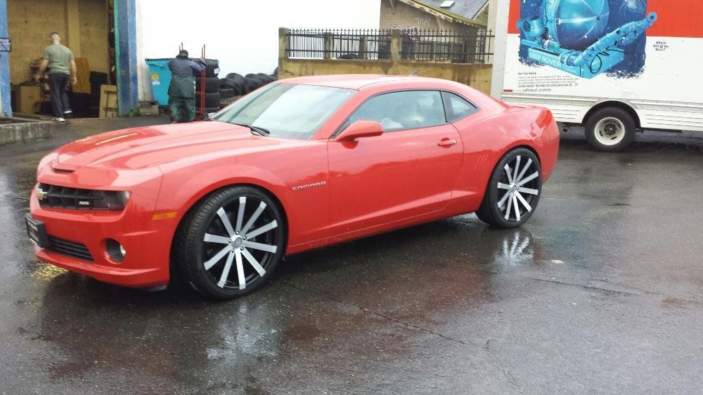 A red car is parked in a parking lot next to a white truck.