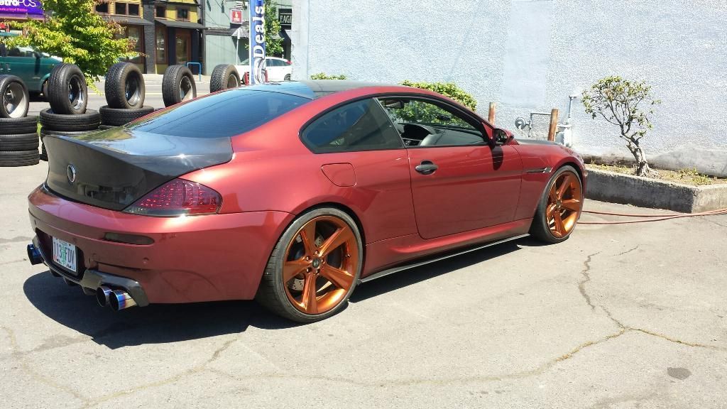 A red sports car is parked in a parking lot next to a pile of tires.