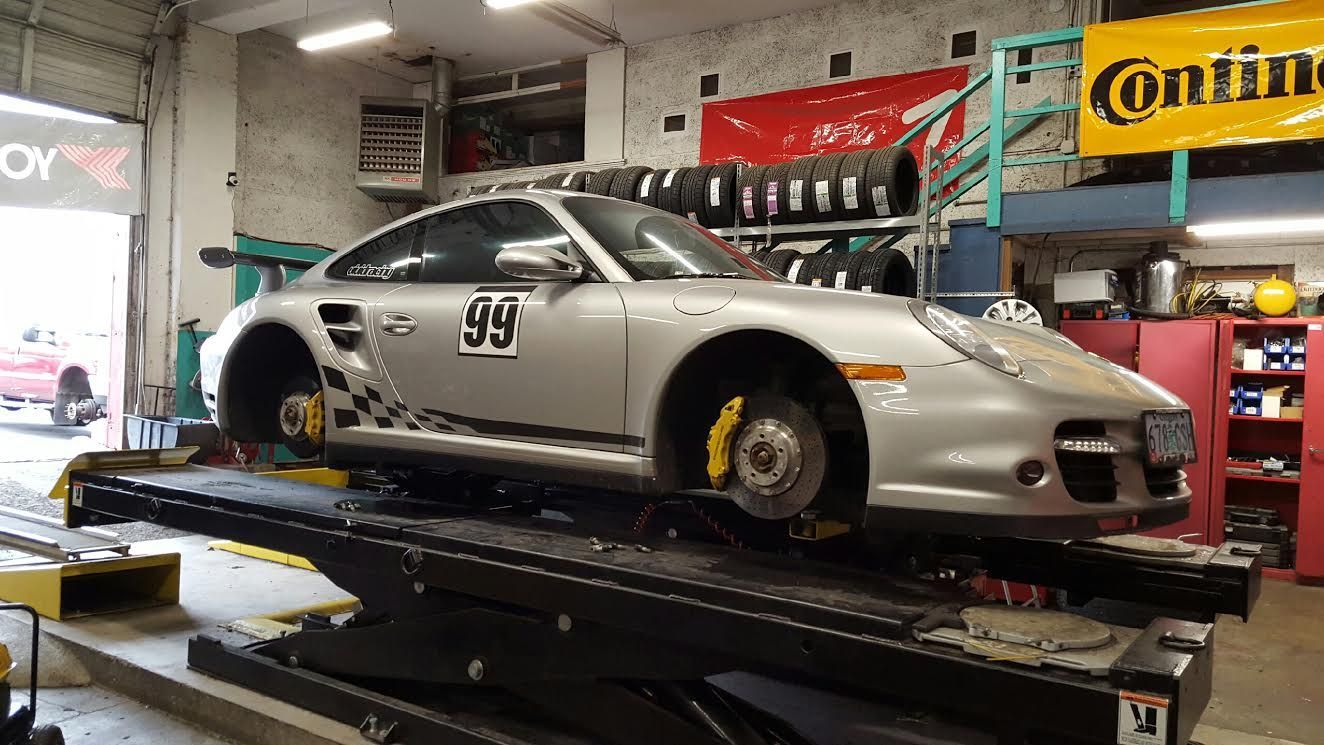 A silver porsche 911 turbo is sitting on a lift in a garage.