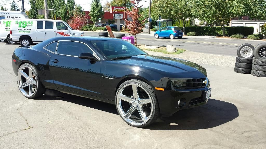 A black car is parked in a parking lot next to a pile of tires.