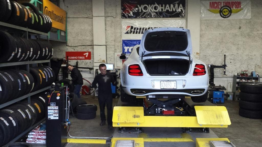 A white car is sitting on a lift in a tire shop.