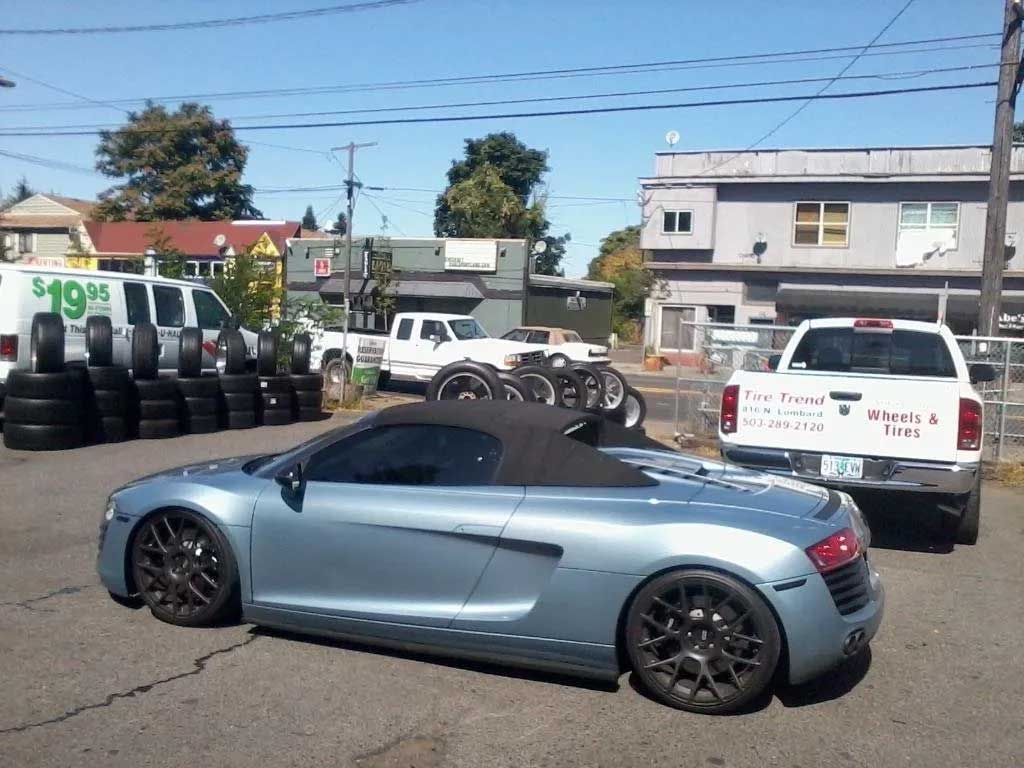 A silver sports car is parked in front of a stack of tires