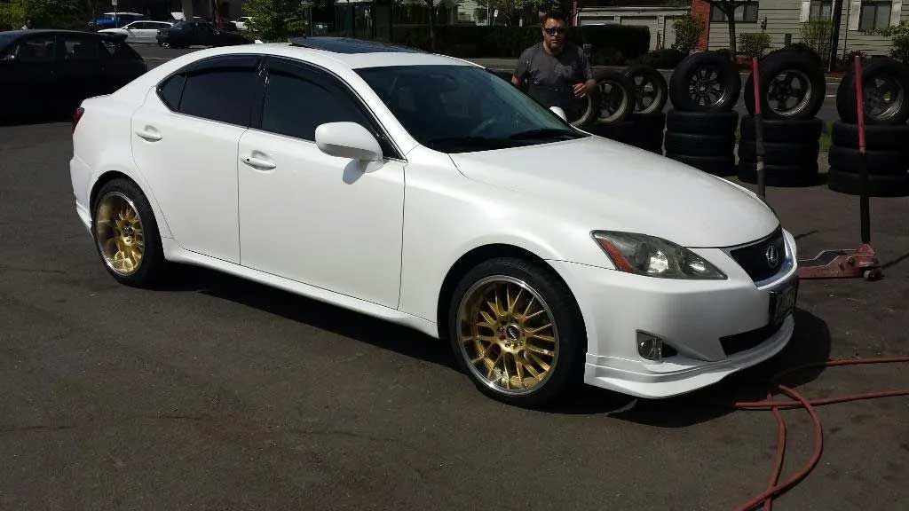 A white car with gold wheels is parked in a parking lot