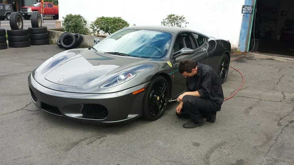 A man is kneeling next to a sports car in a parking lot.