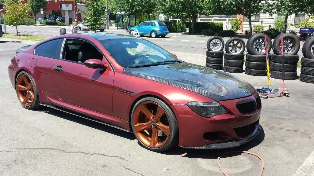 A red car is parked in a parking lot next to a pile of tires