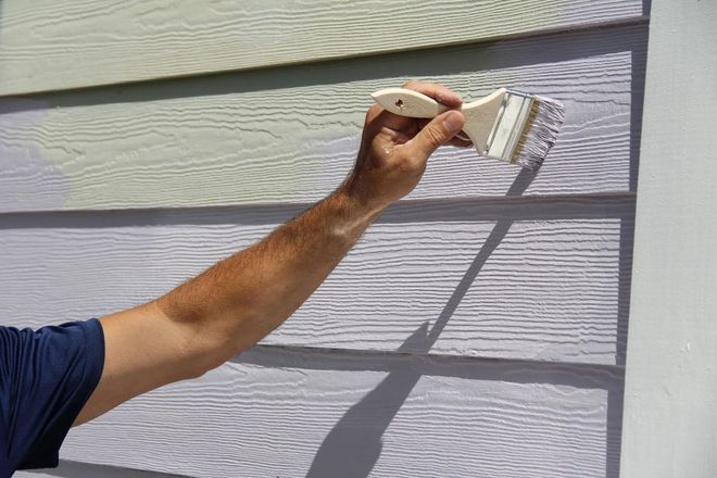 Hand painting white siding on a house exterior with a small brush