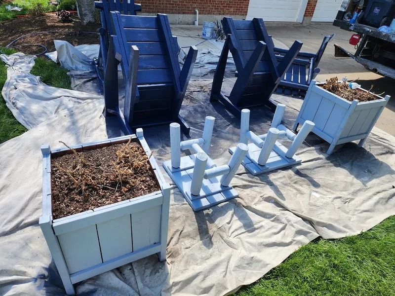 White wooden garden planters and upside-down blue chairs drying on a tarp outdoors