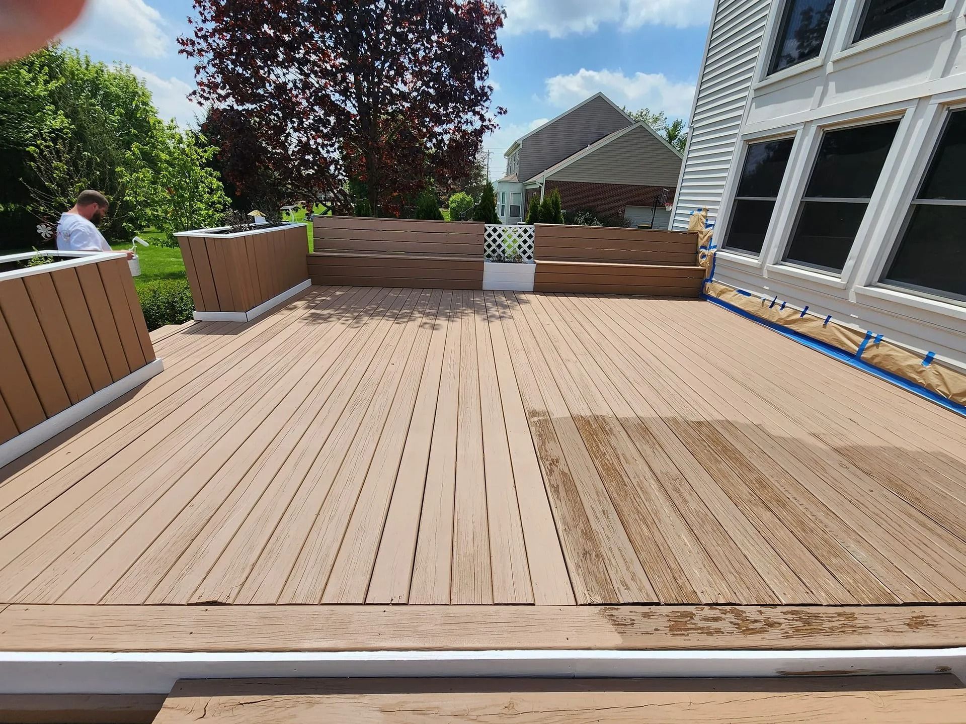 Wooden deck under construction beside a white house, with planters and a person in the background.