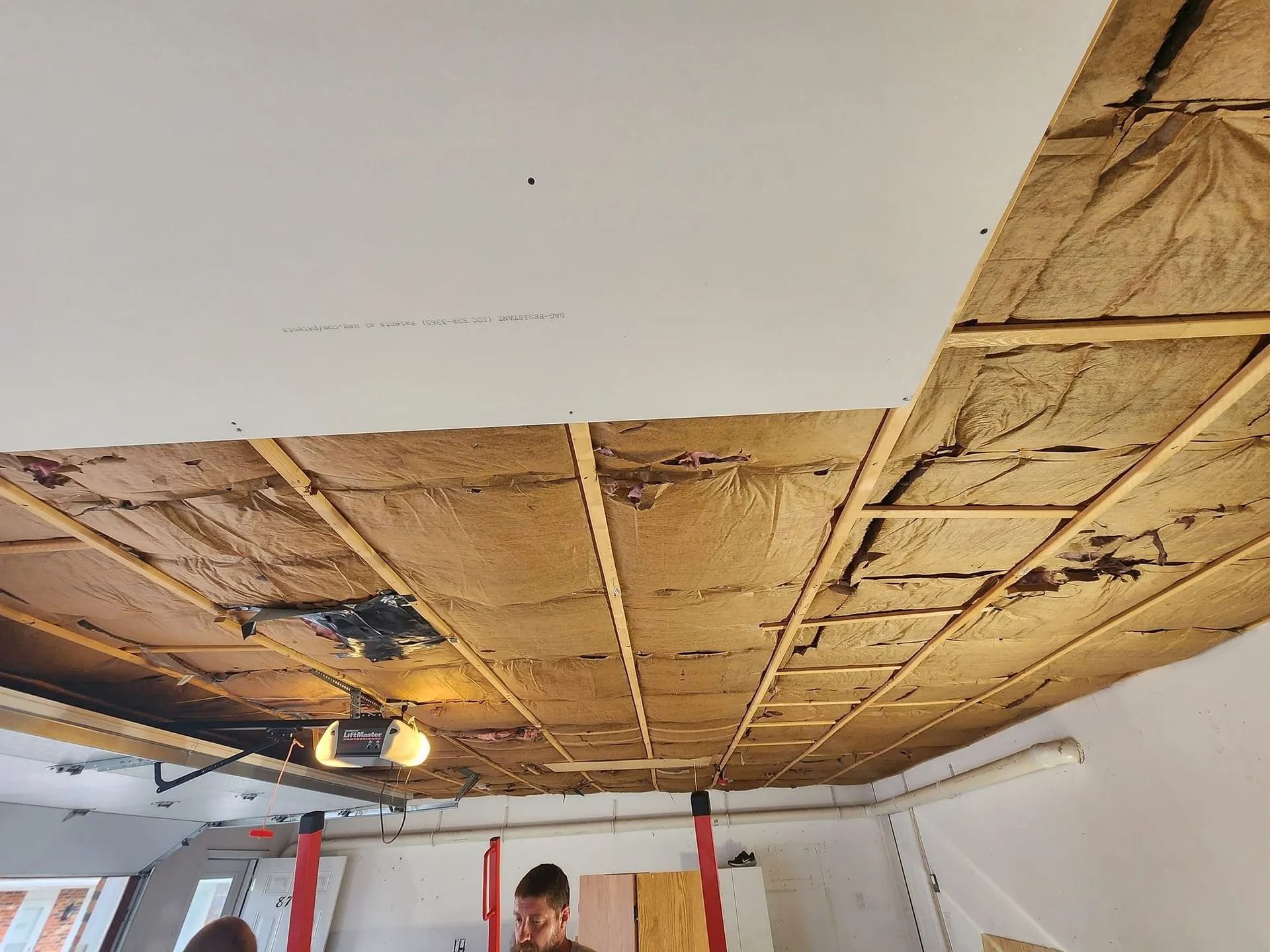 Partially demolished ceiling with exposed insulation and two workers in a room under renovation
