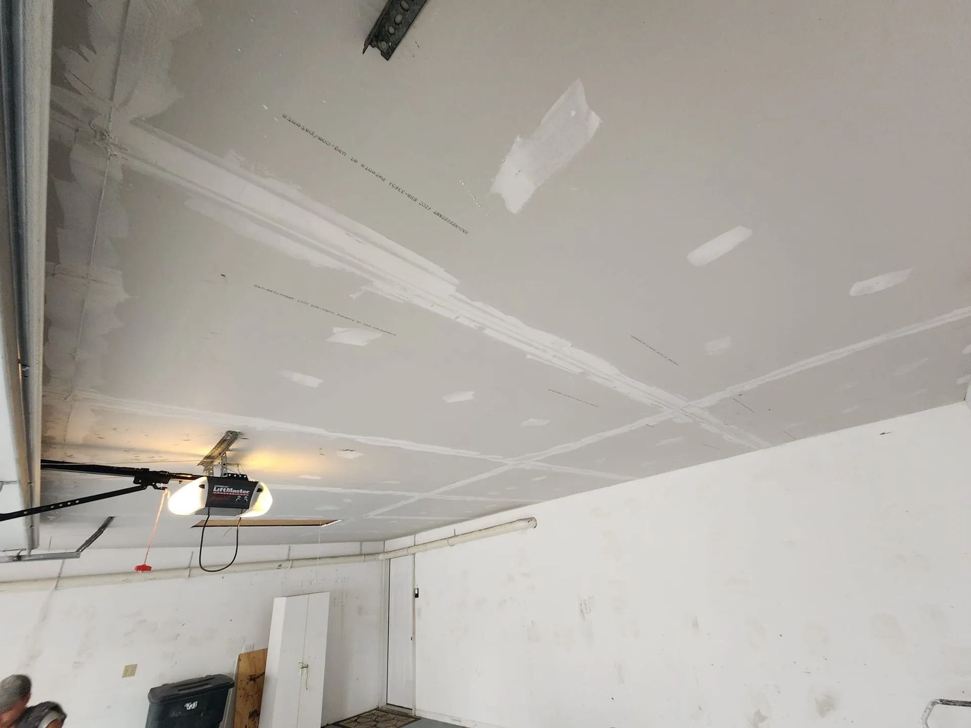 White interior garage under renovation, with unfinished drywall and a ceiling-mounted garage door opener.
