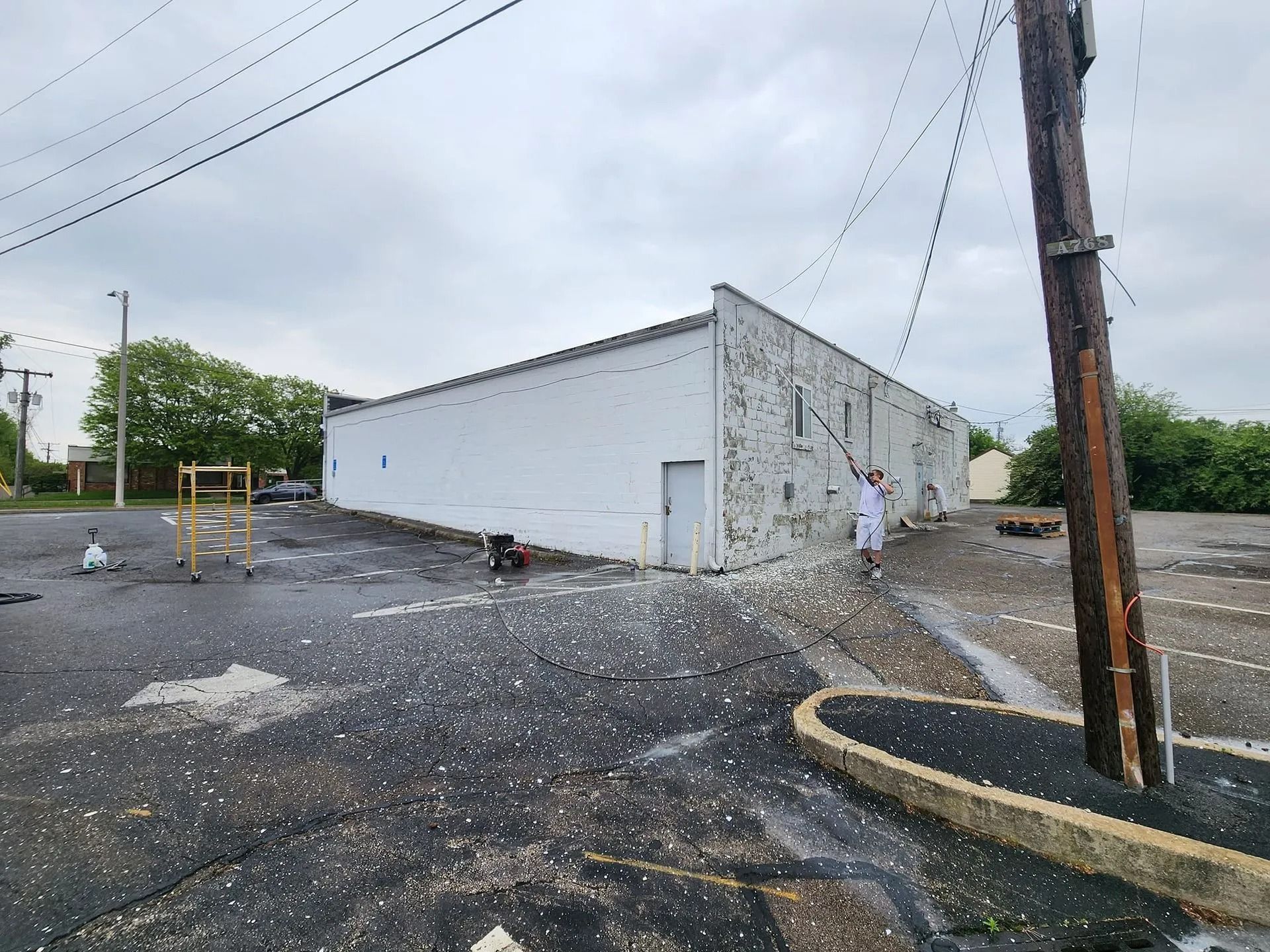 White industrial building in a gravel lot with utility poles and a few people nearby under cloudy skies