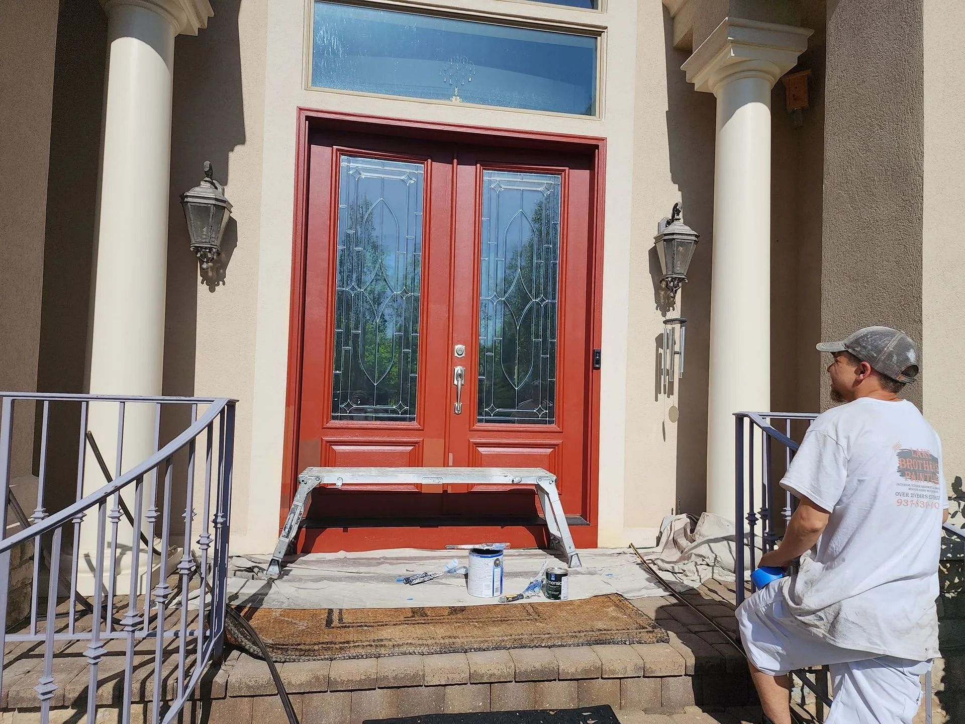 Worker repairing steps at a red front door with columns and a metal railing