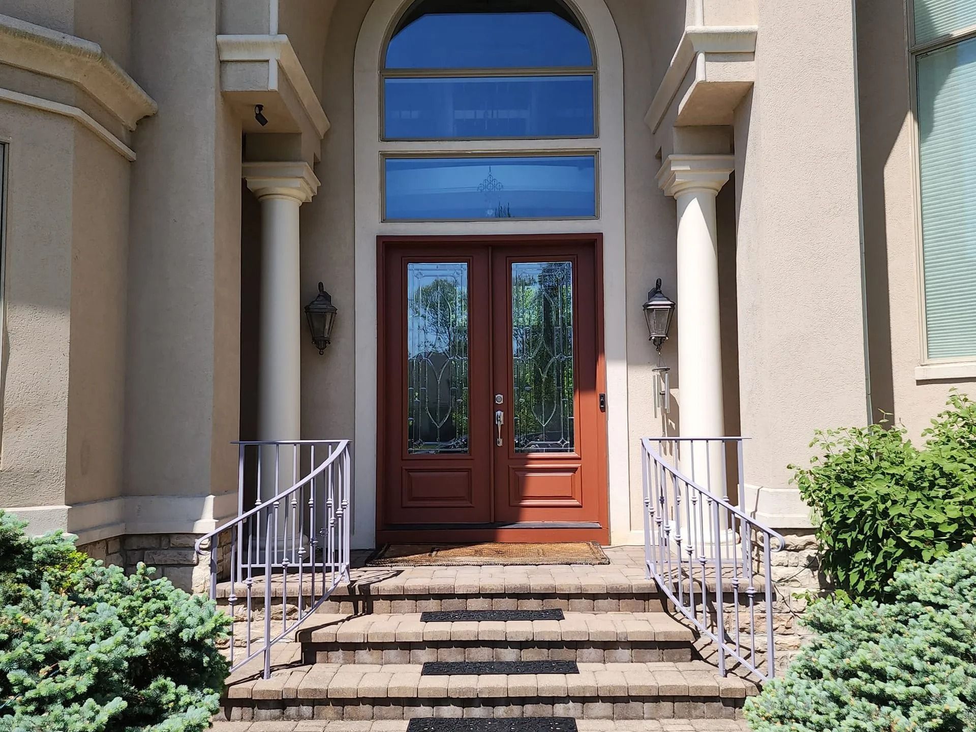 Front entrance with wooden double doors, stone steps, and white railings on a beige building