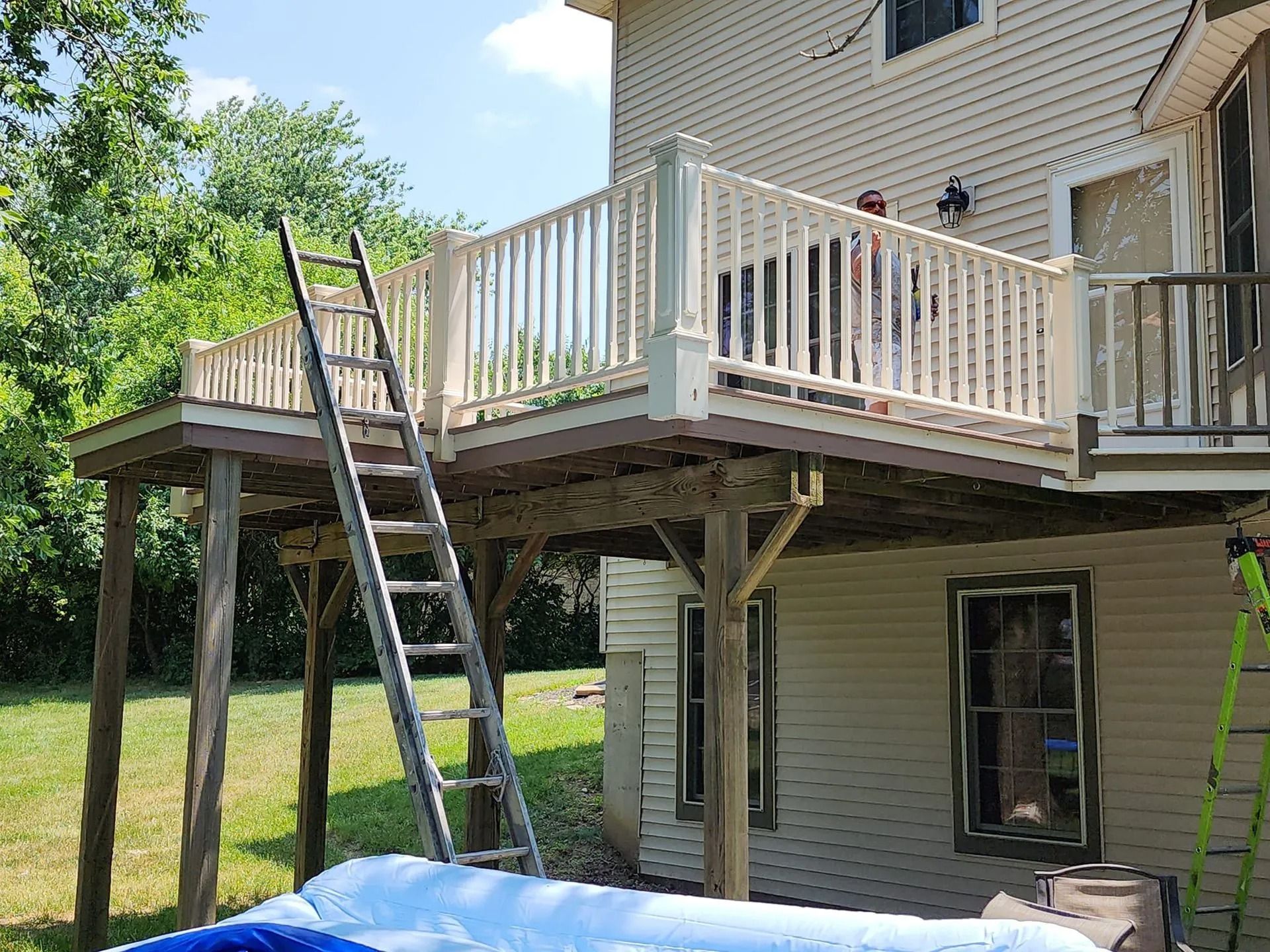 Back deck under construction with ladders leaning against a beige house and white railing