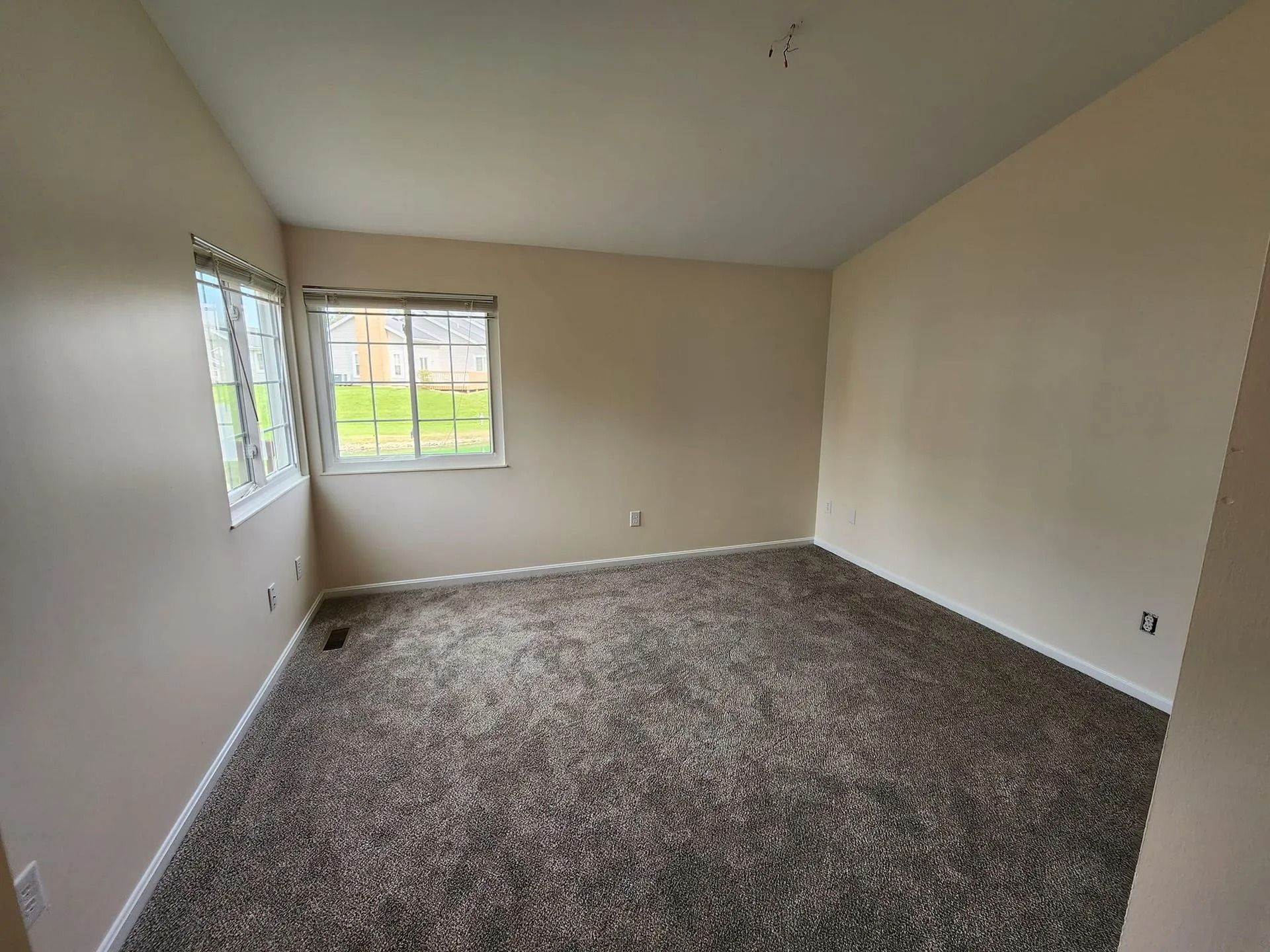 Empty beige bedroom with carpeted floor and two windows