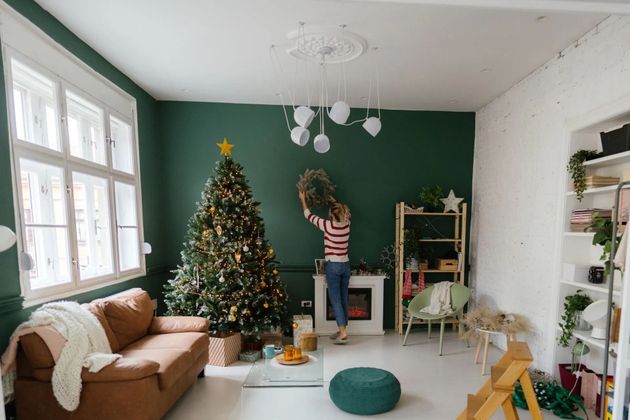 Person decorating a wreath in a cozy living room with a lit Christmas tree and green accent wall