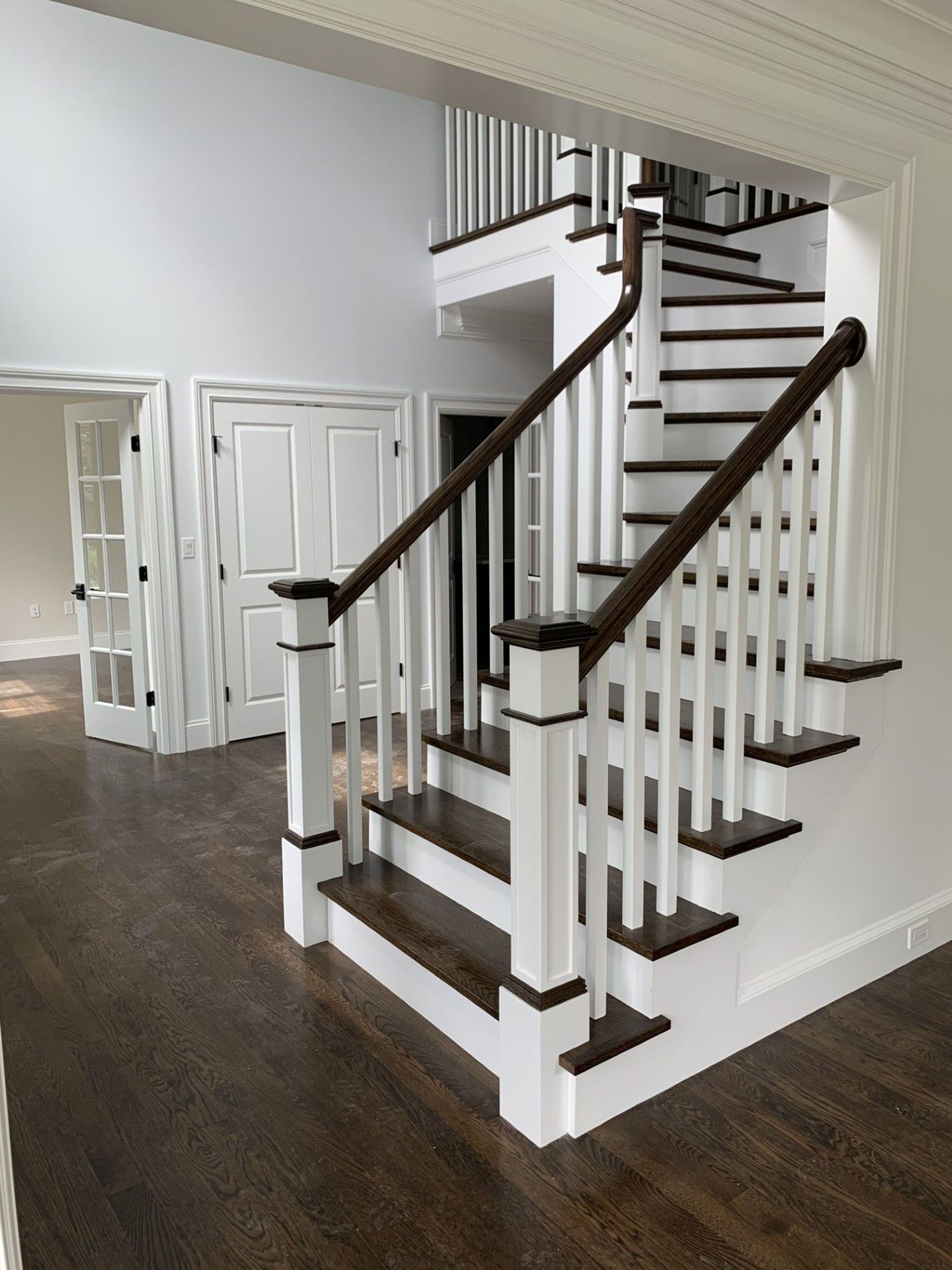 A white staircase with a wooden railing in a house under construction.