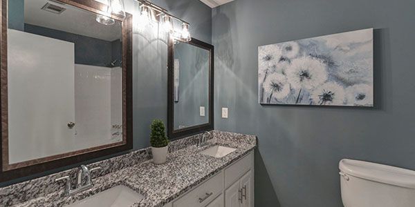 A bathroom with two sinks , a toilet , and a painting on the wall.