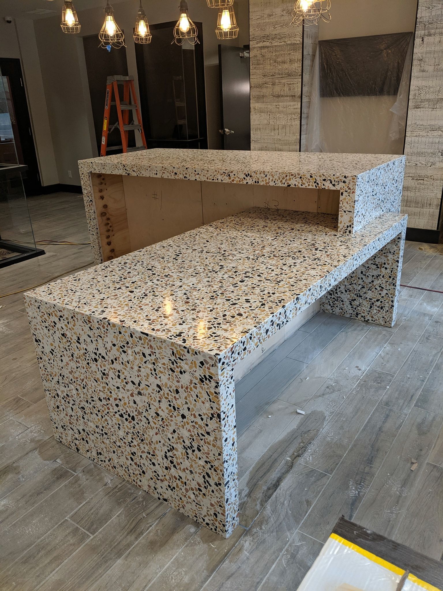 A large granite counter top in a kitchen with a ladder in the background.