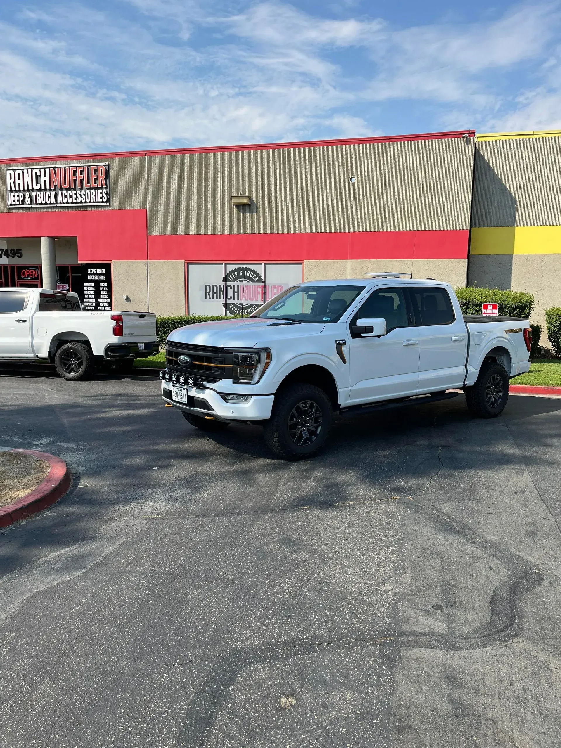 White Ford truck parked in front of a building with red and yellow accents on a sunny day.