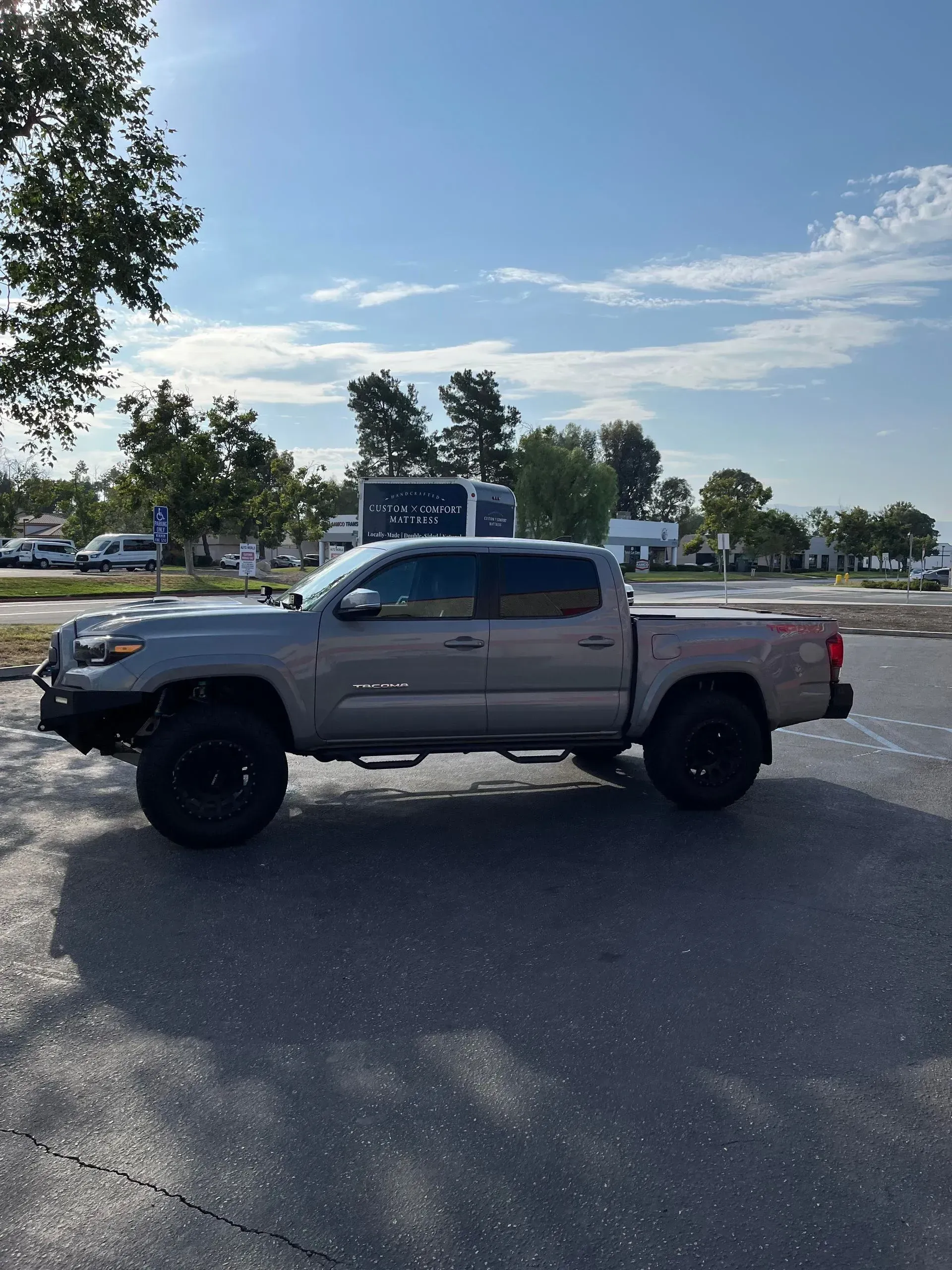 Gray Toyota Tacoma truck with black wheels parked on pavement under a sunny sky.