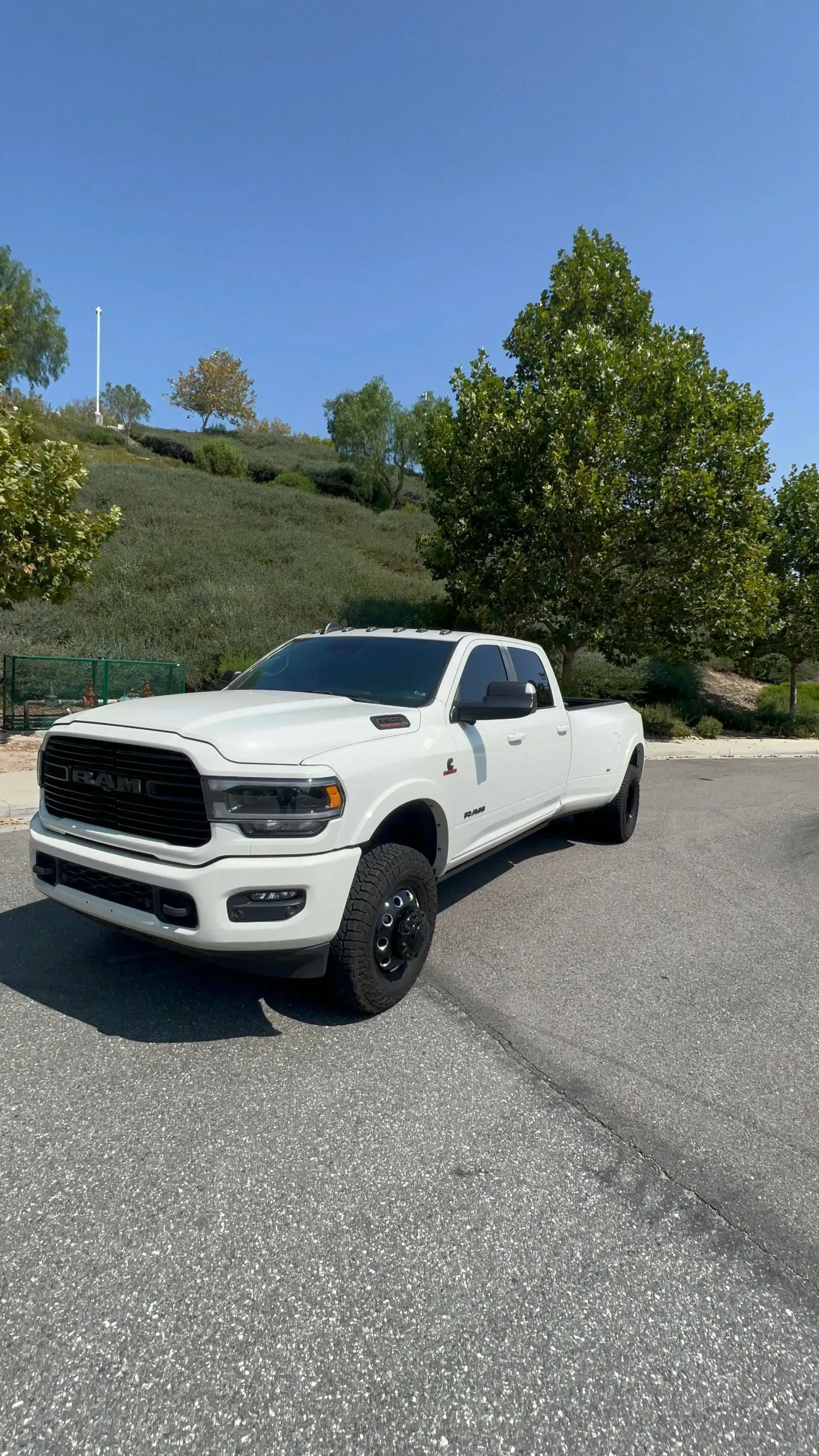 White Ram pickup truck parked on asphalt, against a backdrop of trees and a blue sky.