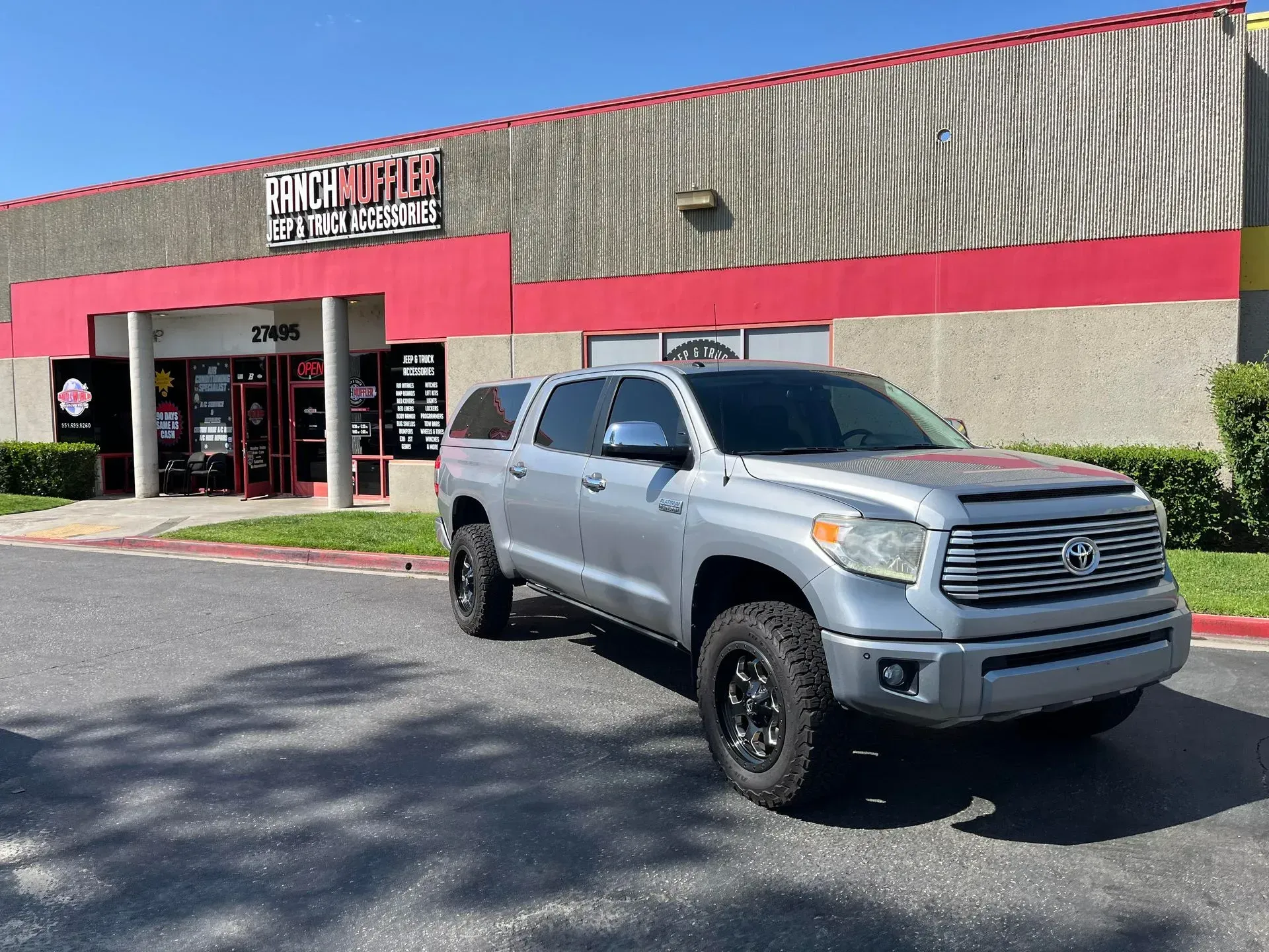 Silver Toyota Tundra pickup truck parked in front of a red and gray building with a business sign.