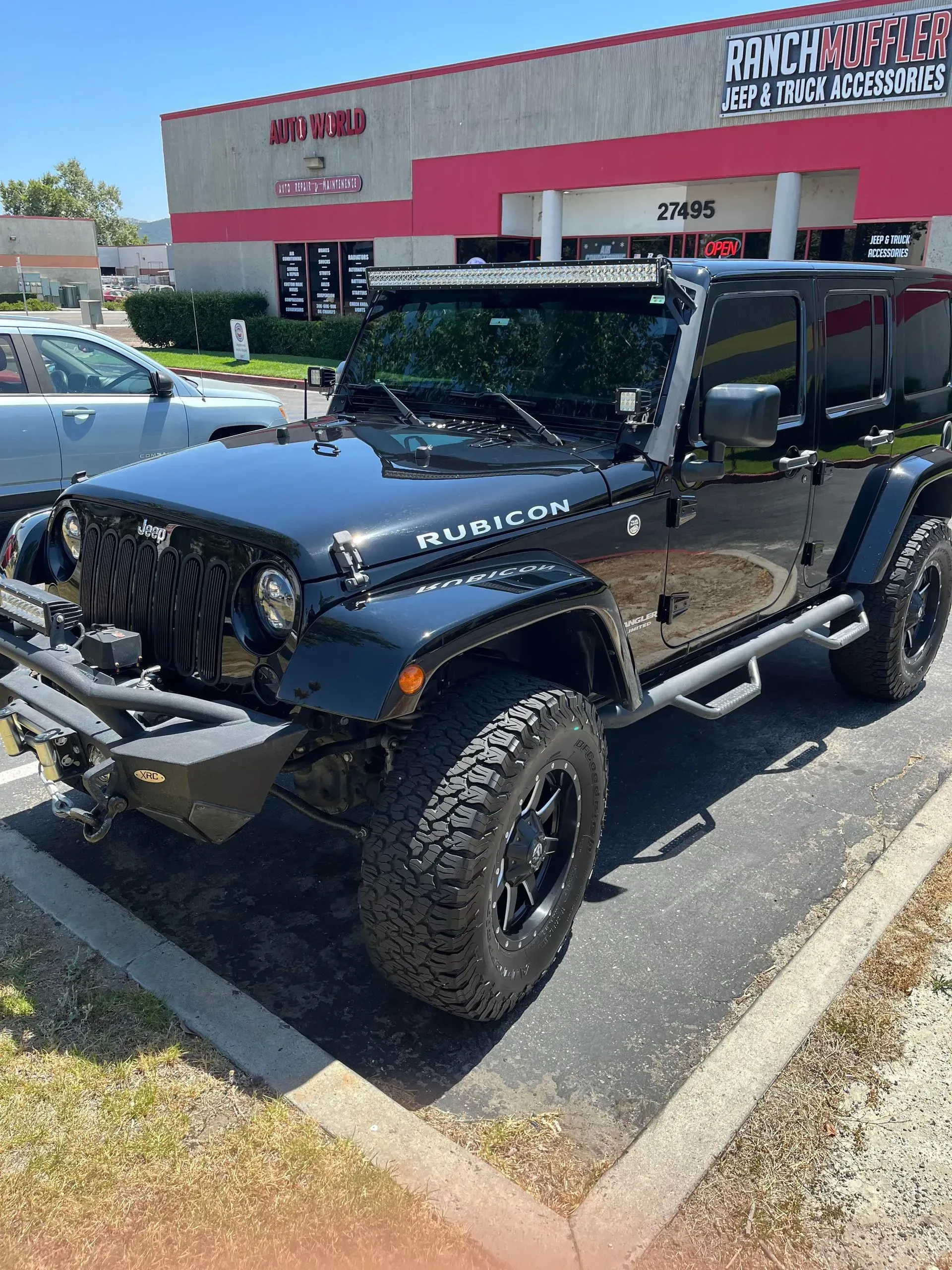 Black Jeep Rubicon parked outside a building on a sunny day.
