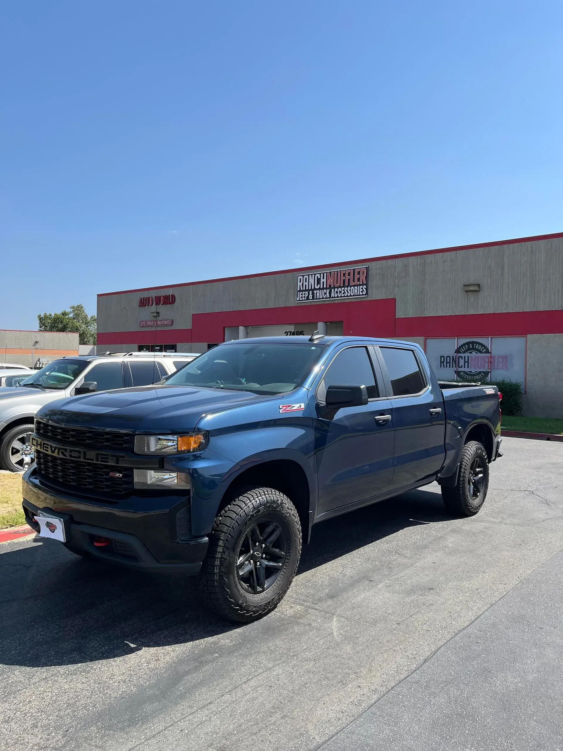 Blue Chevrolet Silverado pickup truck parked on asphalt in front of a building with a red and white sign.