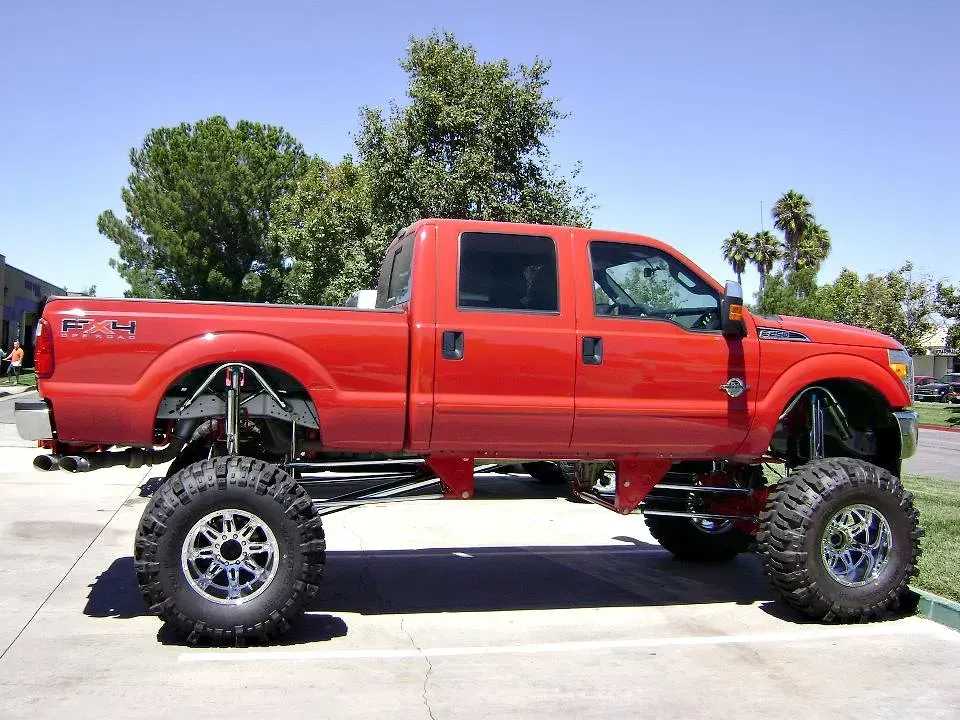 Red lifted pickup truck with large chrome wheels parked outside.