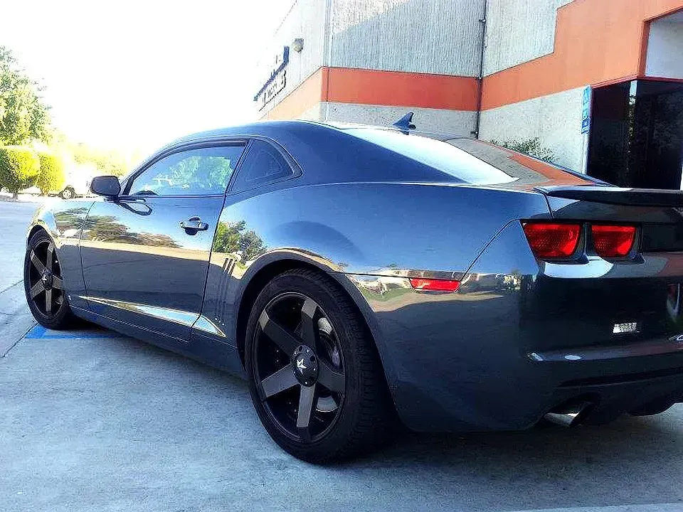 Blue sports car parked outside a building, with black wheels.