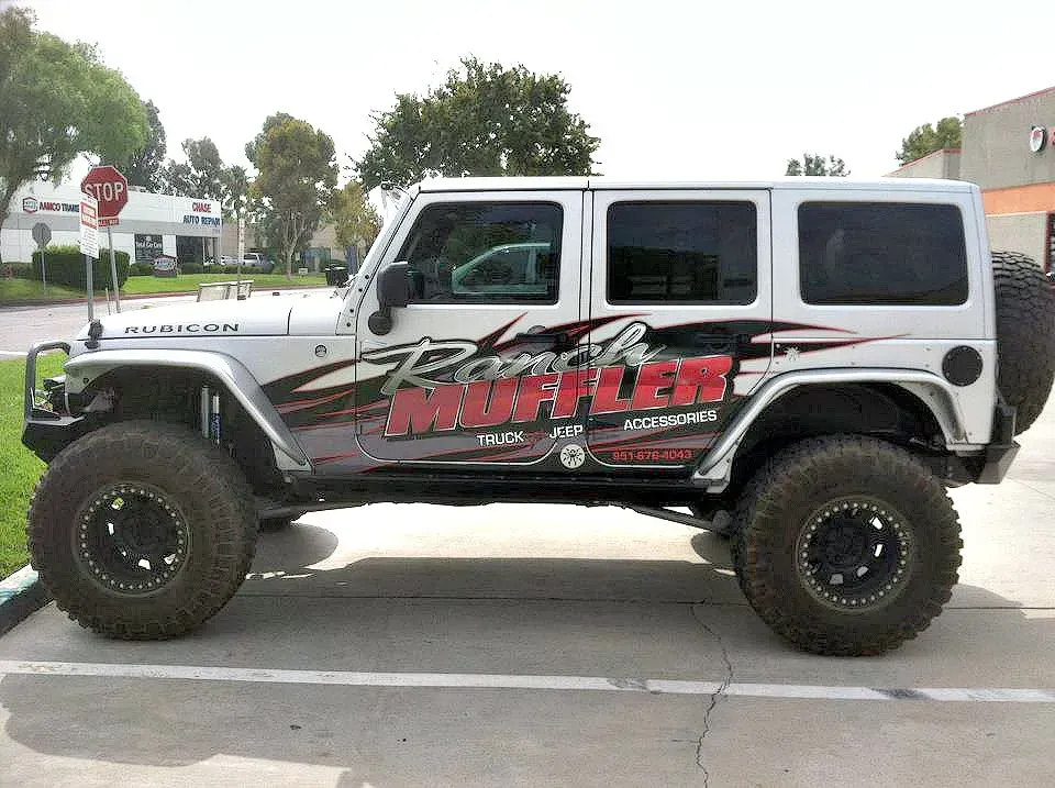 Silver Jeep Wrangler with off-road tires and graphic advertising 