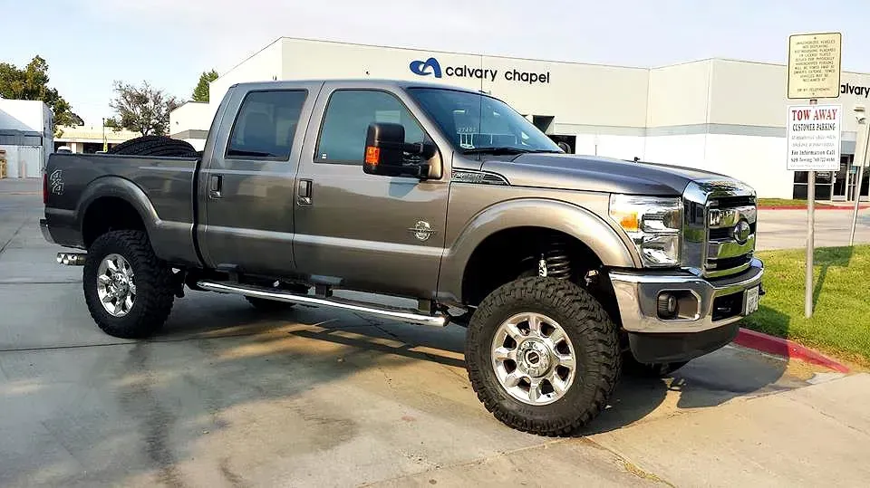 Gray lifted Ford pickup truck parked in front of a building on a sunny day.