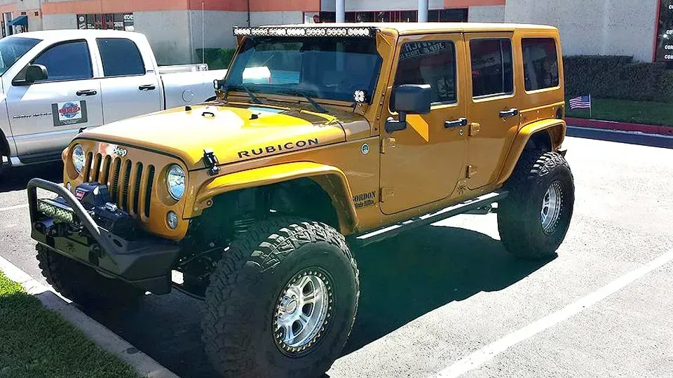 Yellow Jeep Rubicon with large tires and light bar parked outdoors.