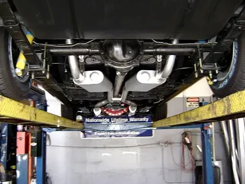 Underside view of a car raised on a lift, showing exhaust system and rear axle.