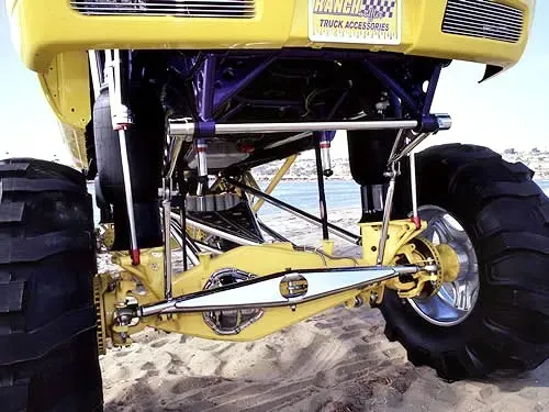 Yellow monster truck suspension, large tires on a beach, against the sky.