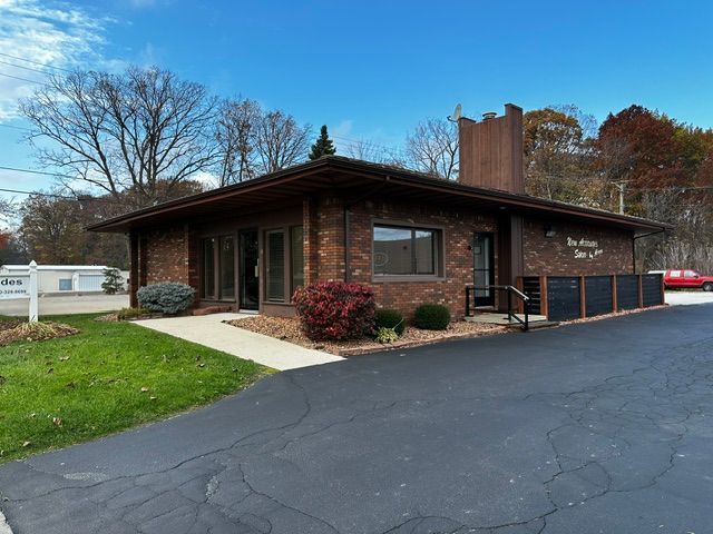 A low-rise, brown brick office building with a chimney and surrounding trees under a blue sky.