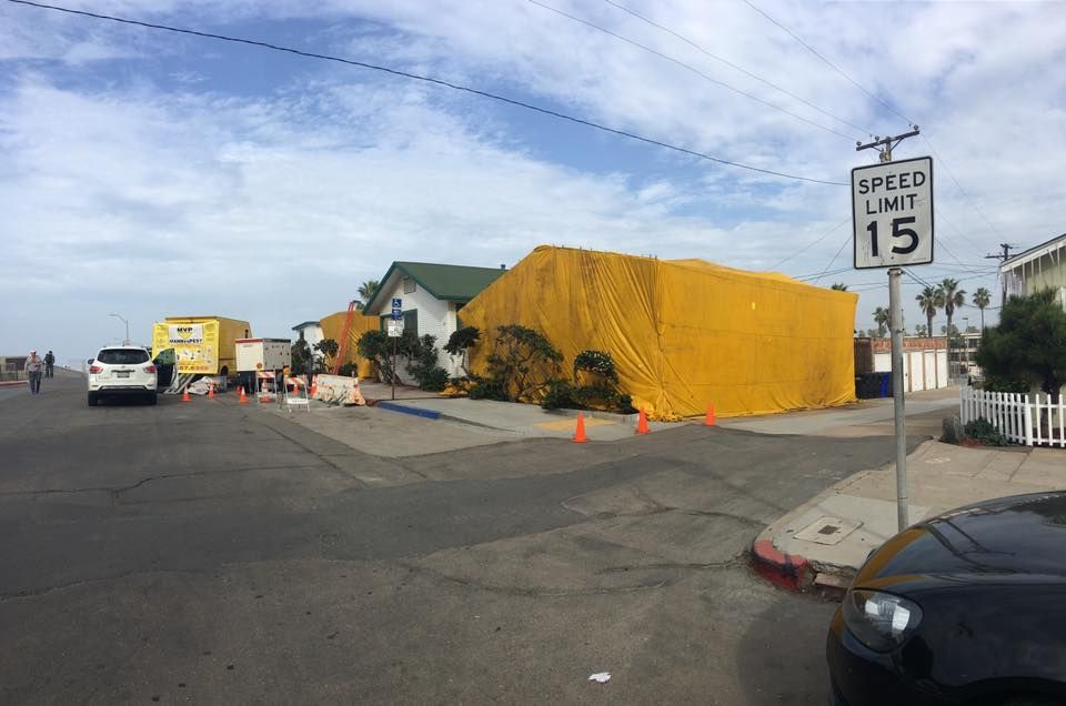 A residential home covered in a large yellow tent for structural fumigation on a sunny street.