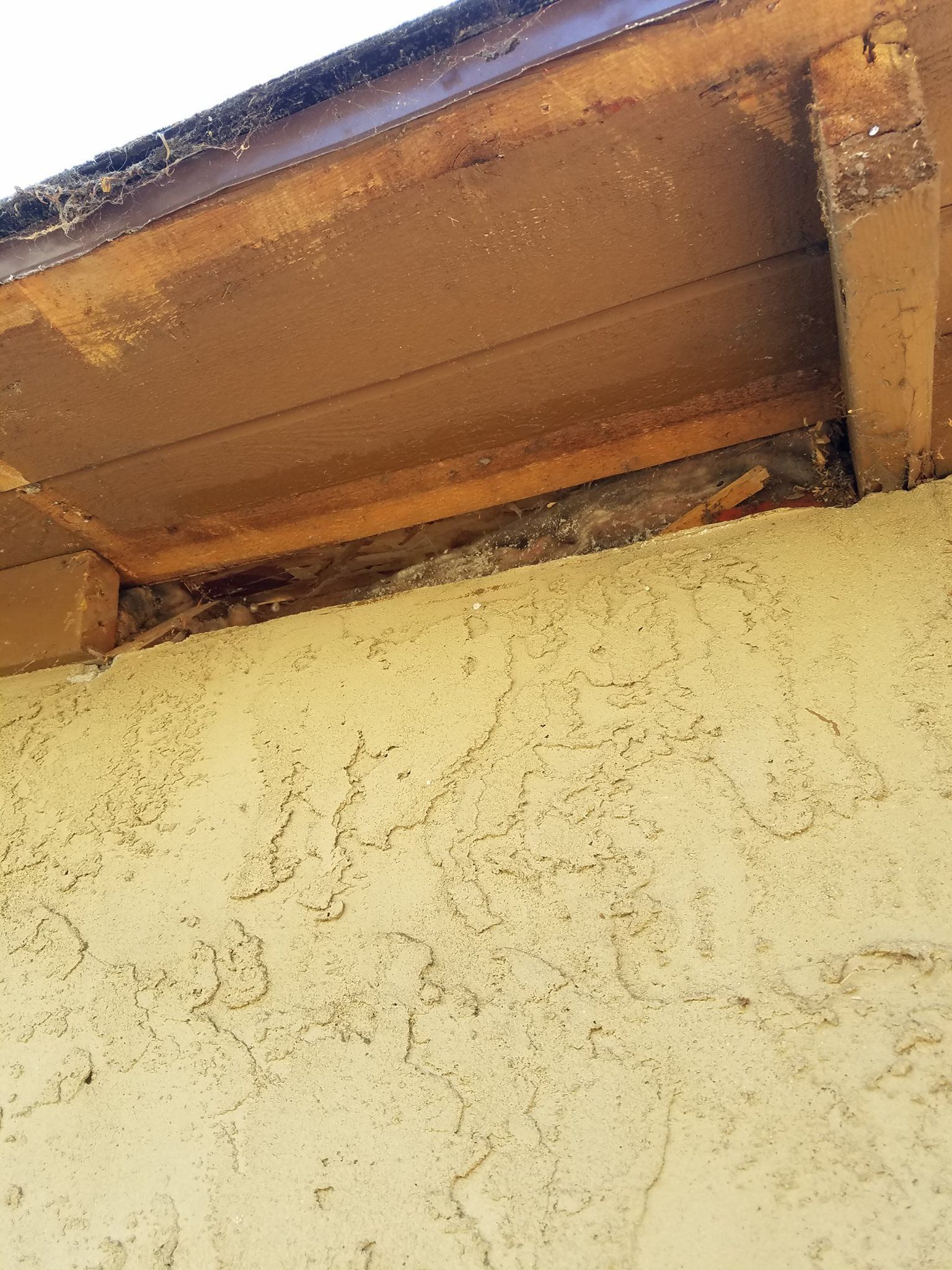 A low-angle view showing a gap between the top of a beige stucco wall and the wooden roof eave or fascia board.