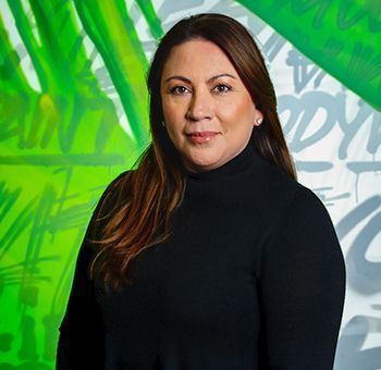 Woman in a black turtleneck smiles, posing in front of a green and white graffiti background.