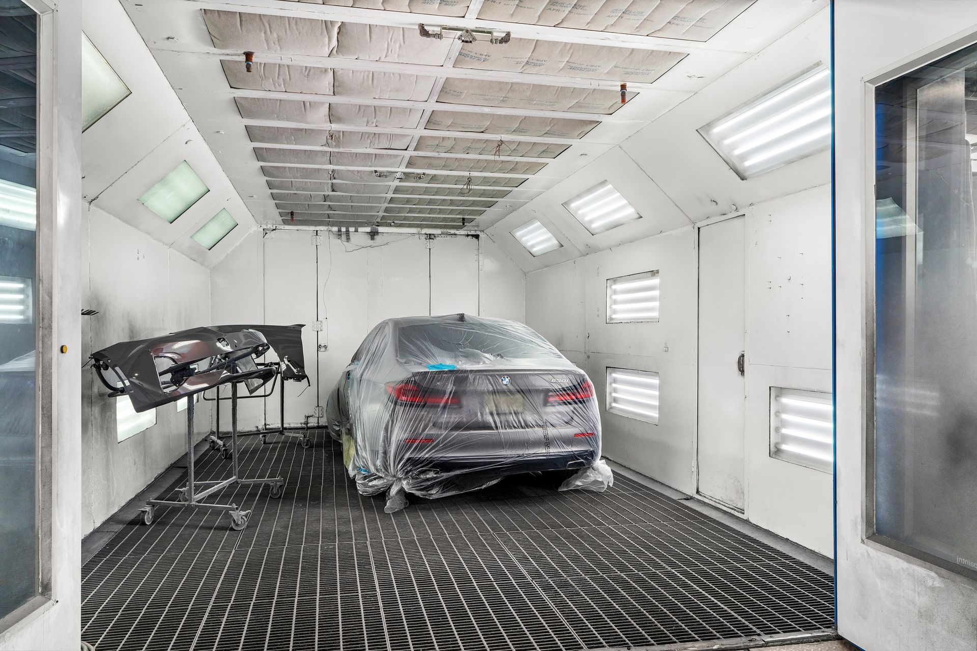 Car in a paint booth covered in plastic, with parts on a stand to the left.